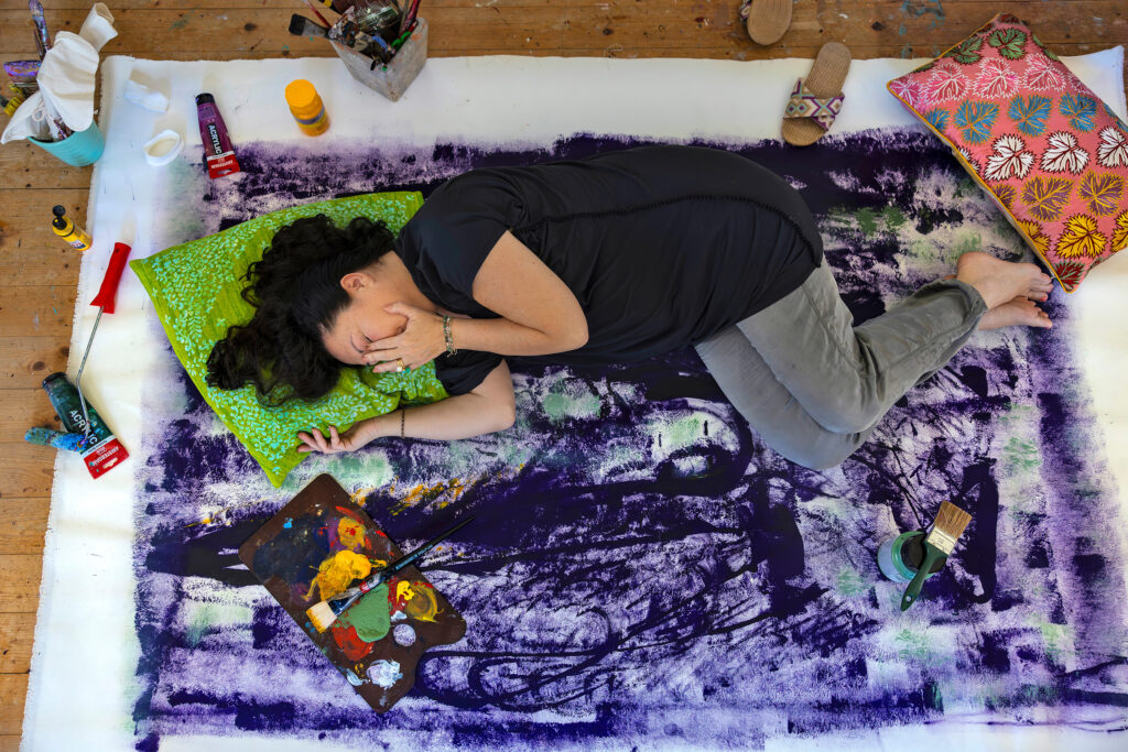 Austria, August 2024: Kornelia Spahn is a former teacher, and painting is her true passion. She has been ill for over 5 years with ME/CFS but still tries to continue with her painting. On good days, she can sit and paint, on most days she must lie down on the canvas and work very slowly. Kornelia has a great deal of pain and often when she tries to paint, she cries as her body fails her. Her sister Sabine is a doctor, and has been a rock for Kornelia, visiting every day and making sure Kornelia has what she needs. Sabine also gives Kornelia regular infustions, which help and make life more bearable for Kornelia. (Photo by Brent Stirton/Getty Images.)